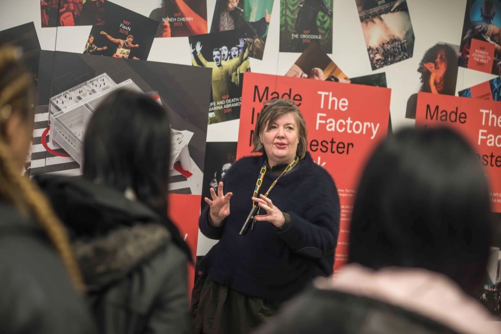 Emma King speaking to students with posters of The Factory and past MIF events behind her